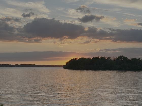 Cayuga Lake with the sun low on the horizon, a wooded point silhouetted against orange sky and the water flat and still
