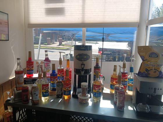 The coffee station in the front window: two dozen flavoring syrups lined up beside the urn, with sprinkles and drizzles alongside