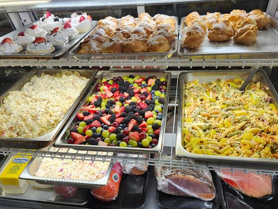 The deli case: trays of mini fruit tarts and cream puffs on the top shelf, macaroni salad, fresh fruit salad and pasta salad below, deli meats on the bottom