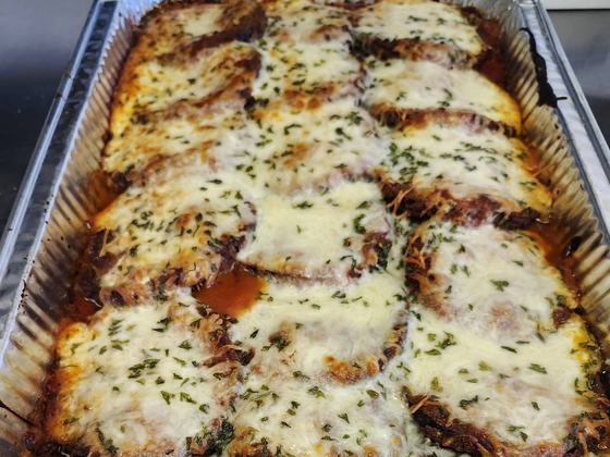 A full tray of baked chicken parmesan, browned mozzarella and parsley over red sauce, straight out of the oven