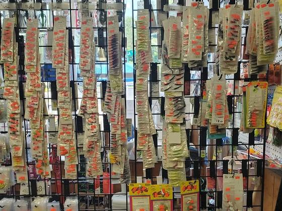 The lure wall: rows of soft plastics and jigs hung on pegboard, every packet hand-marked with its price